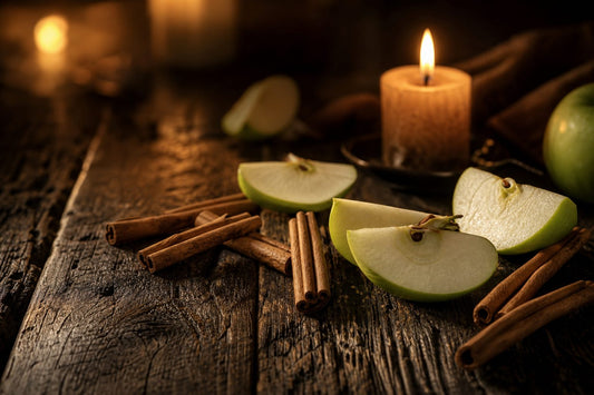 Dark wooden surface with green apple slices and cinnamon sticks illuminated by warm candlelight.